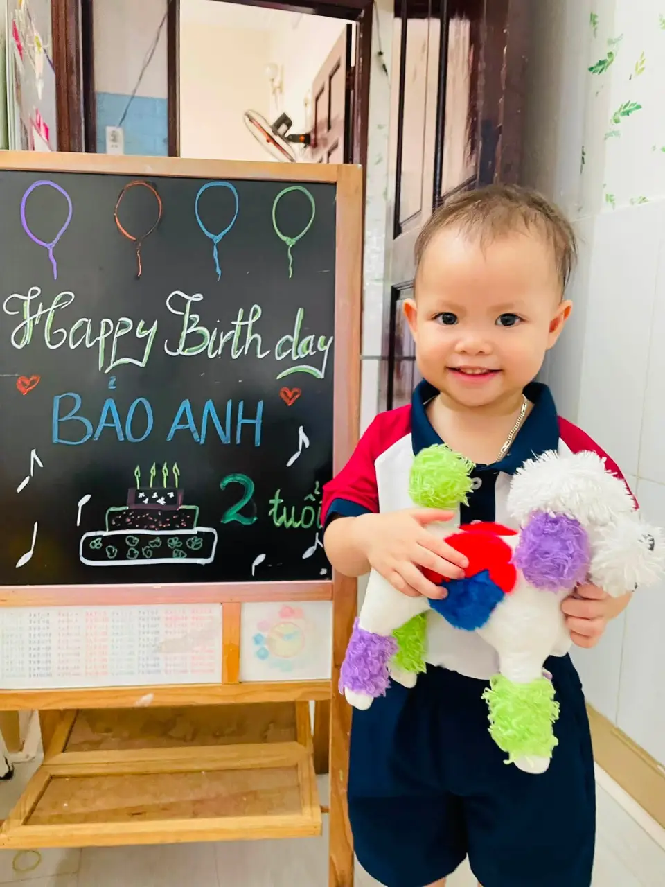 Bé Bảo Anh tạo dáng bên bảng chúc mừng tại lớp học