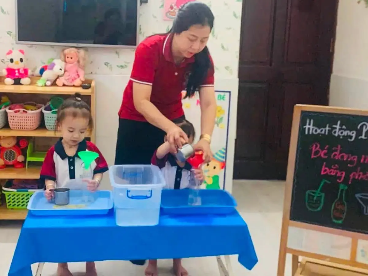 Cô giáo hướng dẫn bé sử dụng phễu trong giờ học
