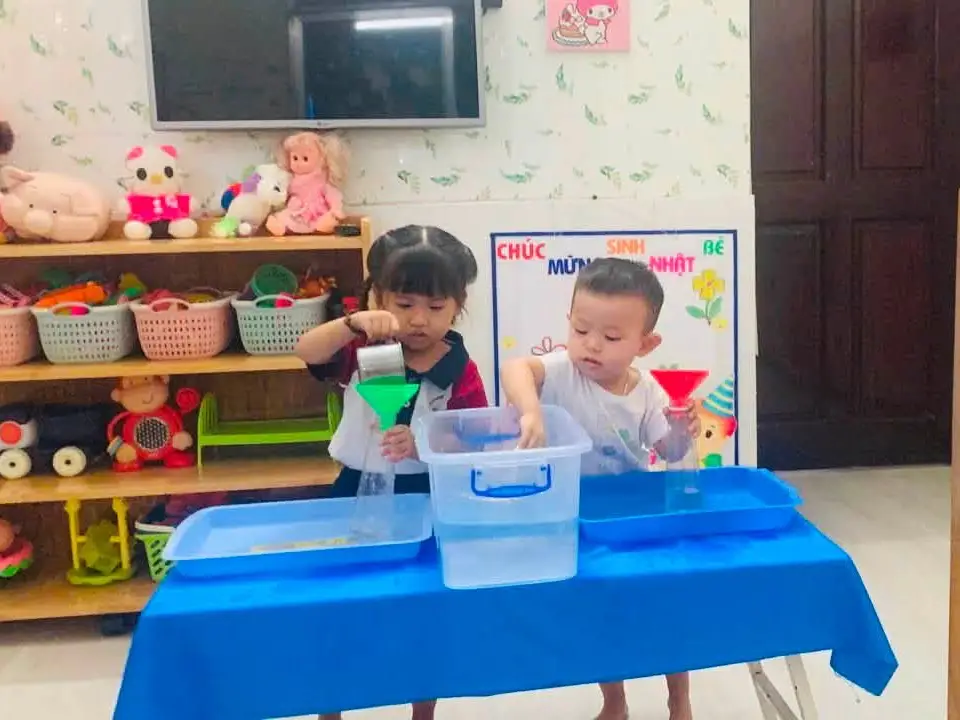 Bé tập trung thực hiện thao tác rót nước bằng phễu