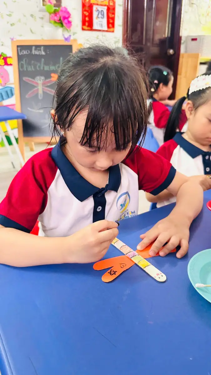 Bé cẩn thận dán các bộ phận của chú chuồn chuồn